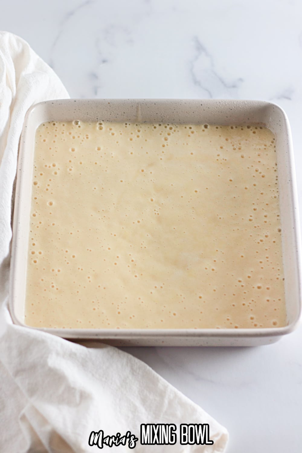 raw cake batter poured into a square white baking dish ready to go in the oven