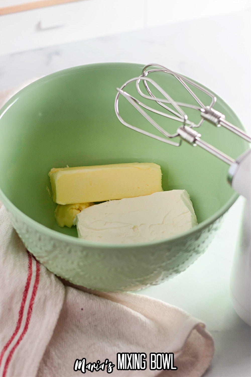 cream cheese and butter being beaten with a hand mixer in a green mixing bowl