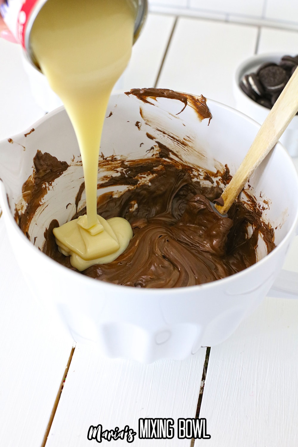 sweetened condensed milk being poured into melted chocolate in a mixing bowl