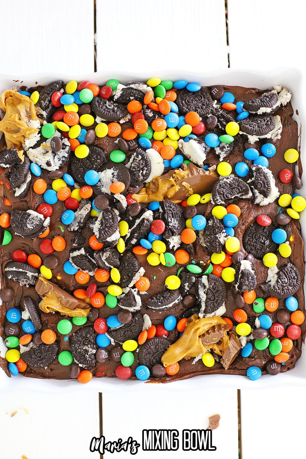 oreo's, m&M's and peanut butter cups on top of chocolate fudge in a parchment lined baking dish