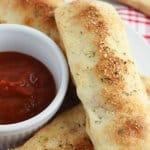 three stuffed breadsticks on a white plate with a bowl of pizza sauce