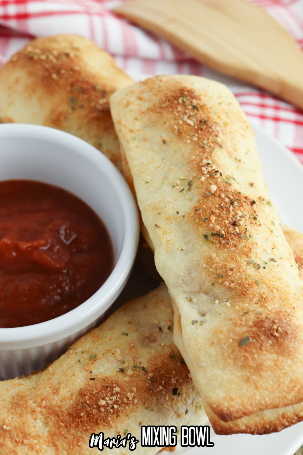 three stuffed breadsticks on a white plate with a bowl of pizza sauce