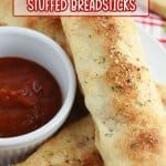three stuffed breadsticks on a white plate with a bowl of pizza sauce