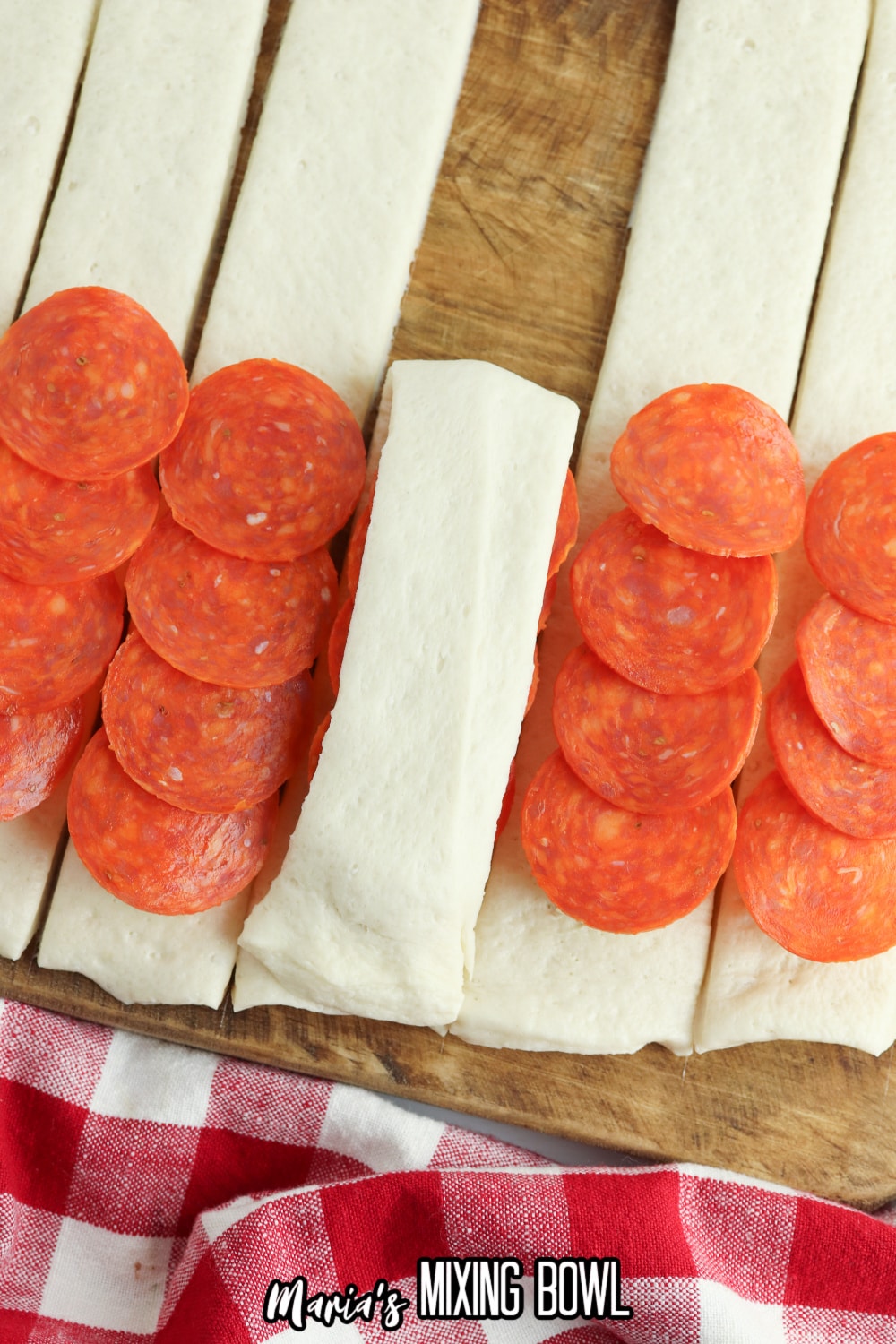 pepperoni and cheese being added to breadsticks on a wooden cutting board