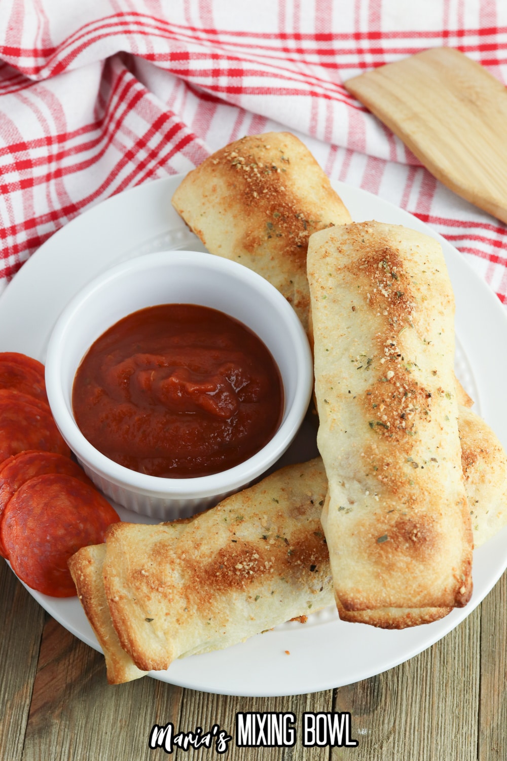 three stuffed breadsticks on a white plate with a bowl of pizza sauce