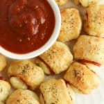 puff pastry pizza bites on a white plate with a bowl of marinara sauce