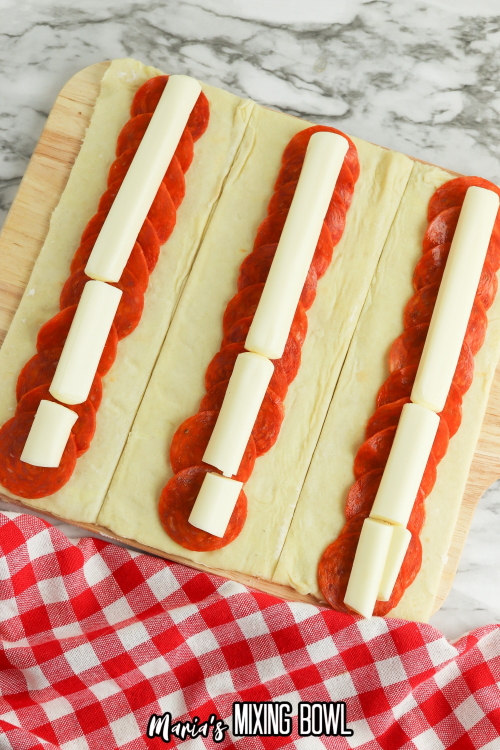 puff pastry being stuffed with pepperoni and string cheese on a wooden cutting board
