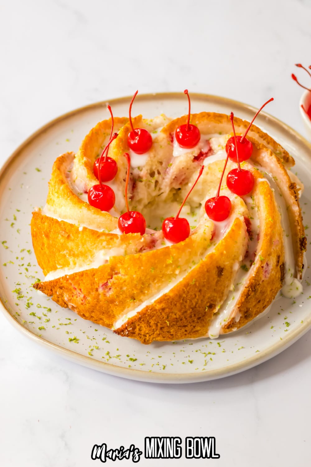 uncut Shirley temple cake topped with glaze and cherries on a white and gold plate