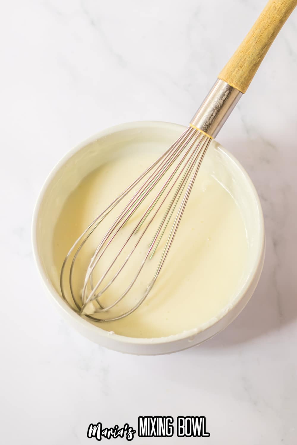 glaze being made in a small white bowl with a whisk with a wooden handle laying on the top