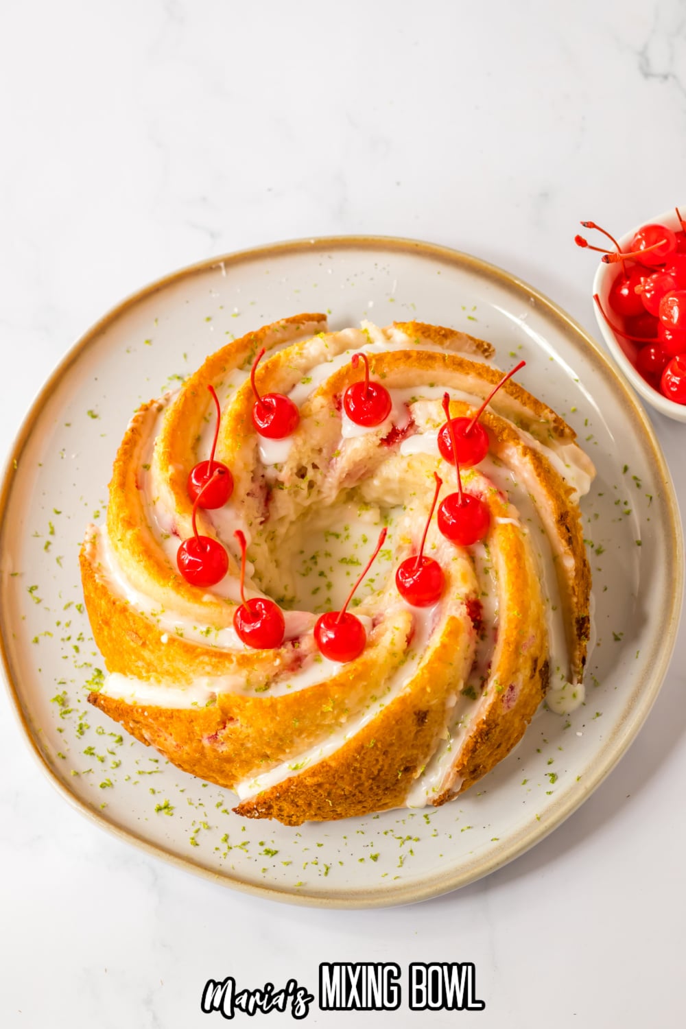uncut Shirley temple cake topped with glaze and cherries on a white and gold plate