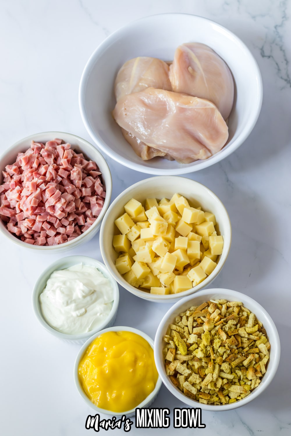 bowls of raw chicken breasts, diced ham, diced cheese, sour cream, cream of chicken soup, and dry stuffing mixing