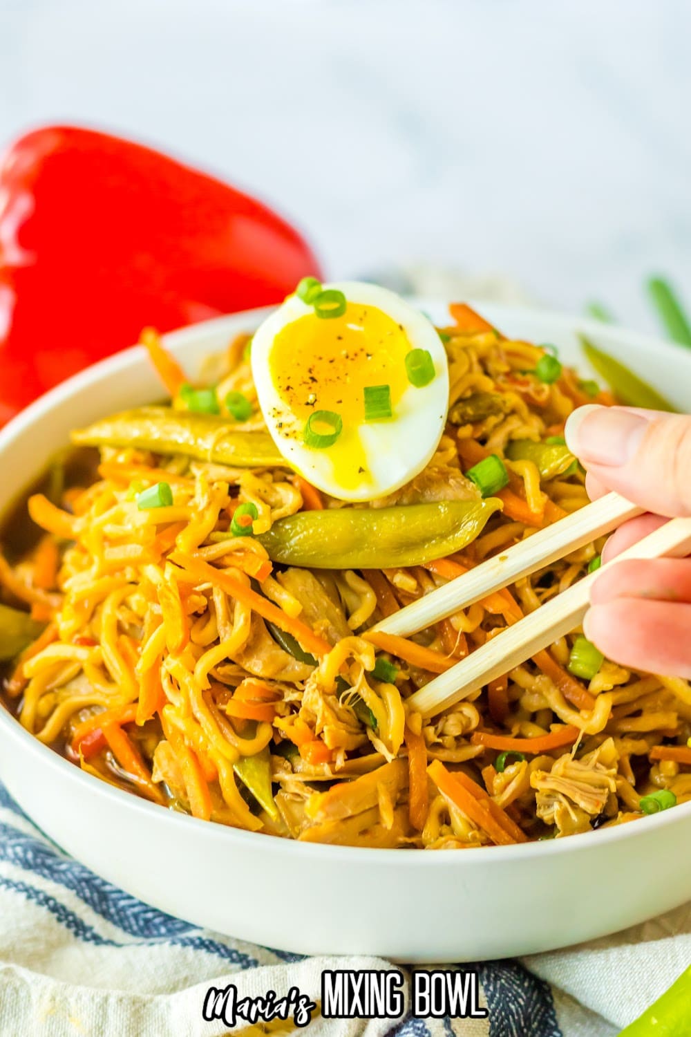 close up of a bowl of chicken ramen with a bite being removed with chopsticks