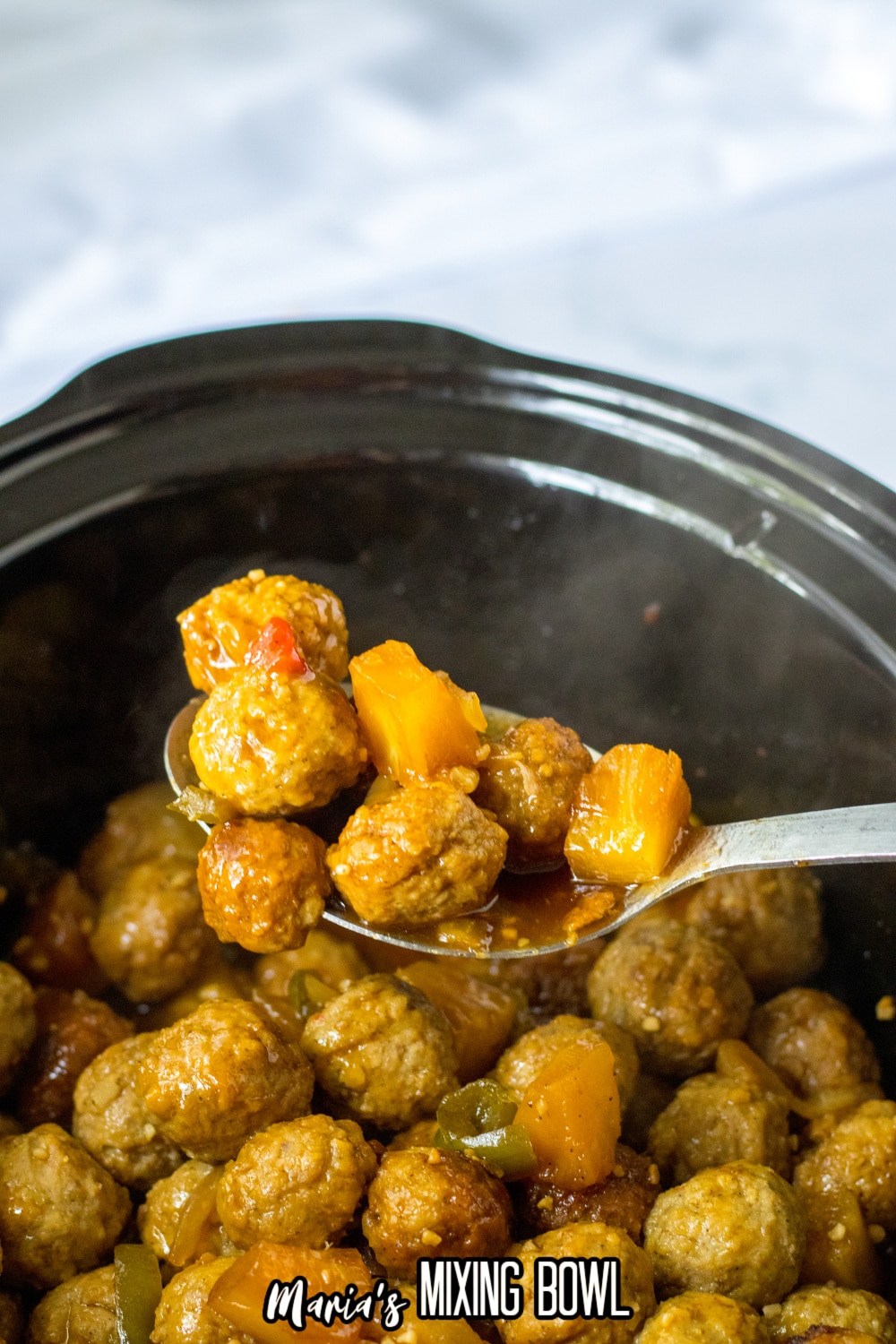 large metal spoon full of hawaiian meatballs held above a slow cooker