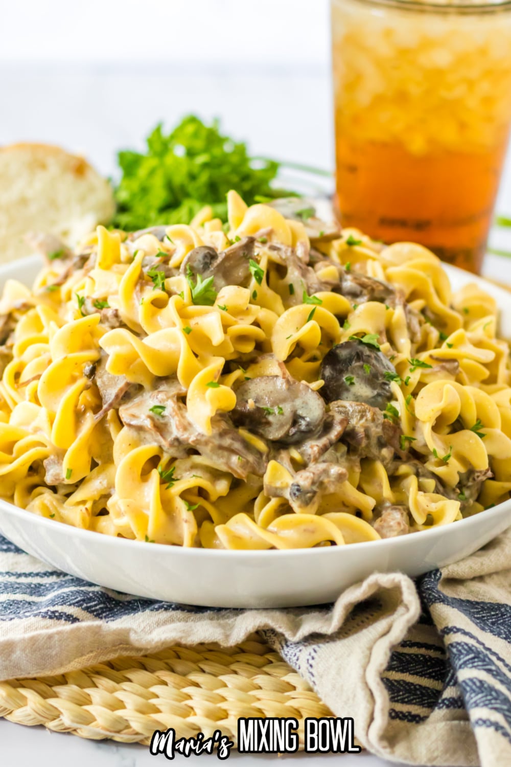 white bowl filled with slow cooker pot roast stroganoff with a glass of iced tea in the background