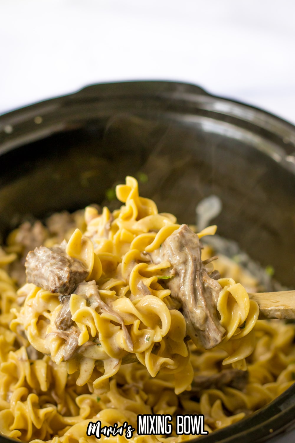 large wooden spoonful of pot roast stroganoff held in the air above the slow cooker