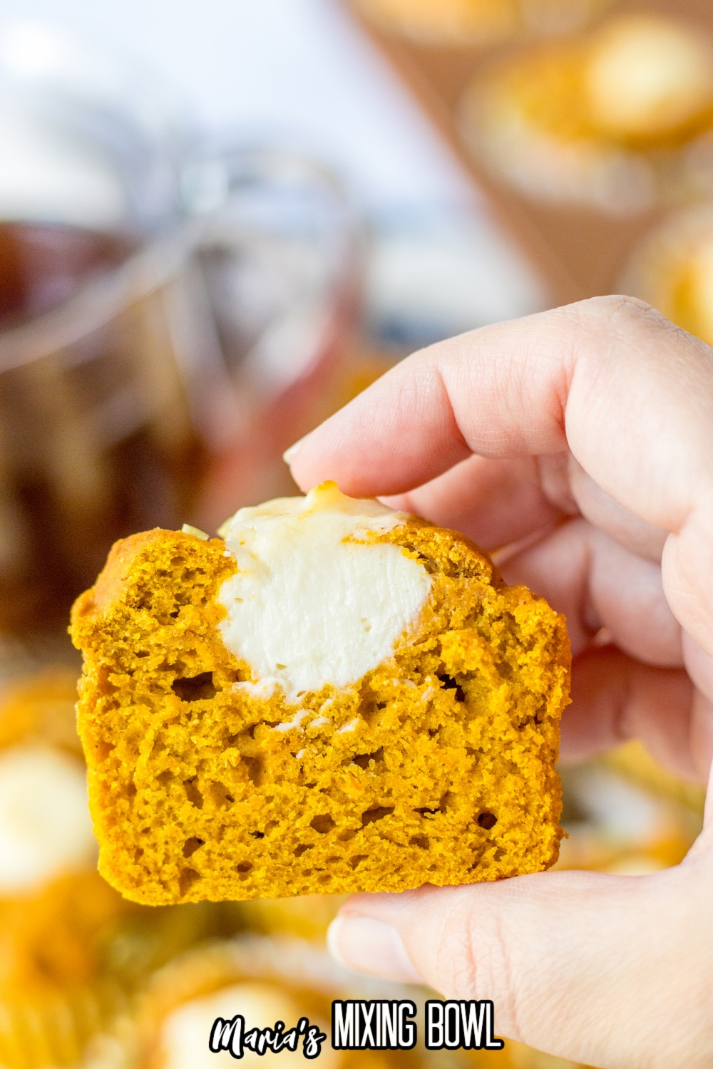 half of a pumpkin muffin with a cream cheese center held in the air in a woman's hand.