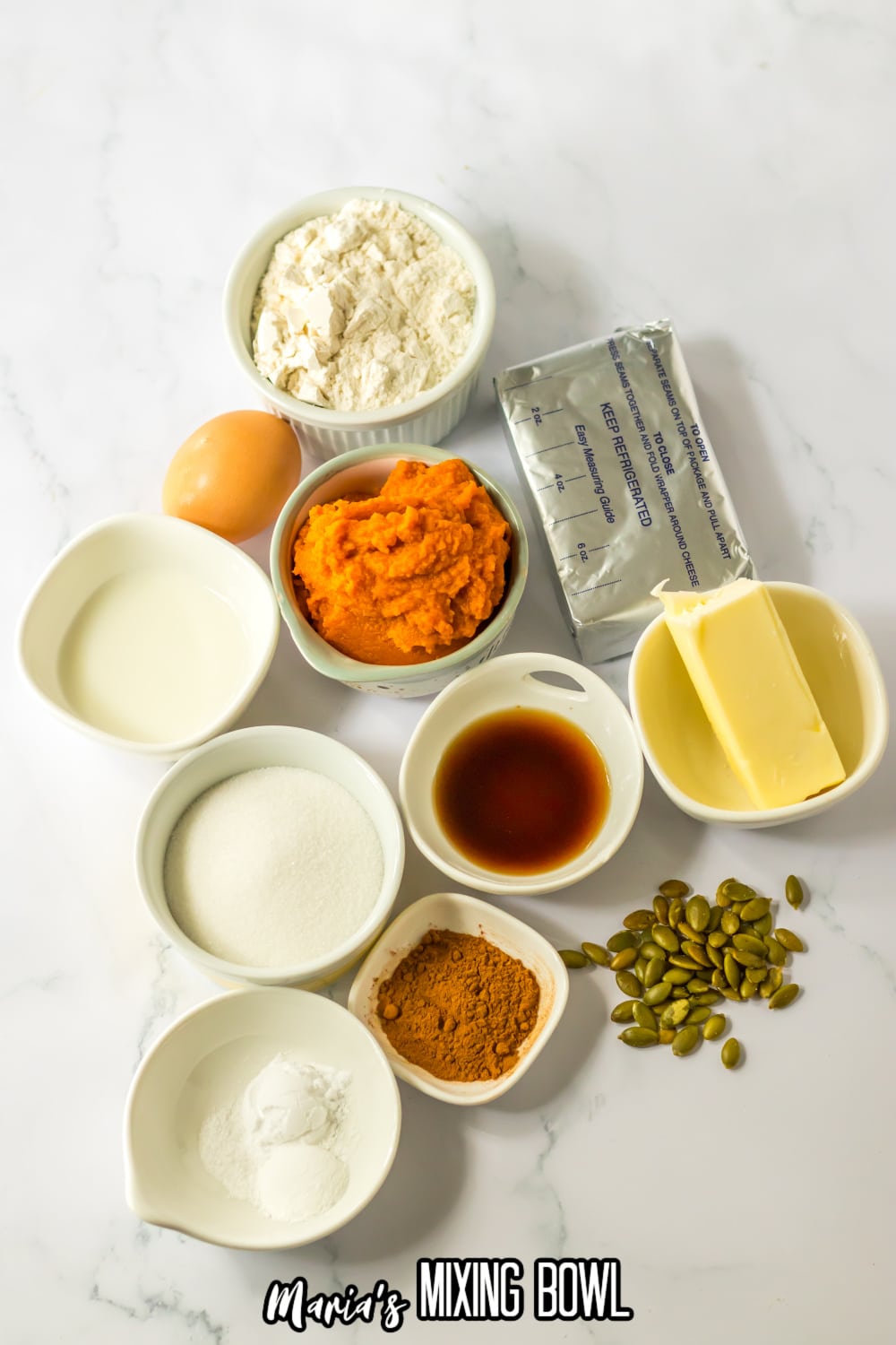 bowls of flour, granulated sugar, pumpkin puree, vanilla, pumpkin pie spice, butter salt, baking powder, baking soda, and pumpkin seeds.