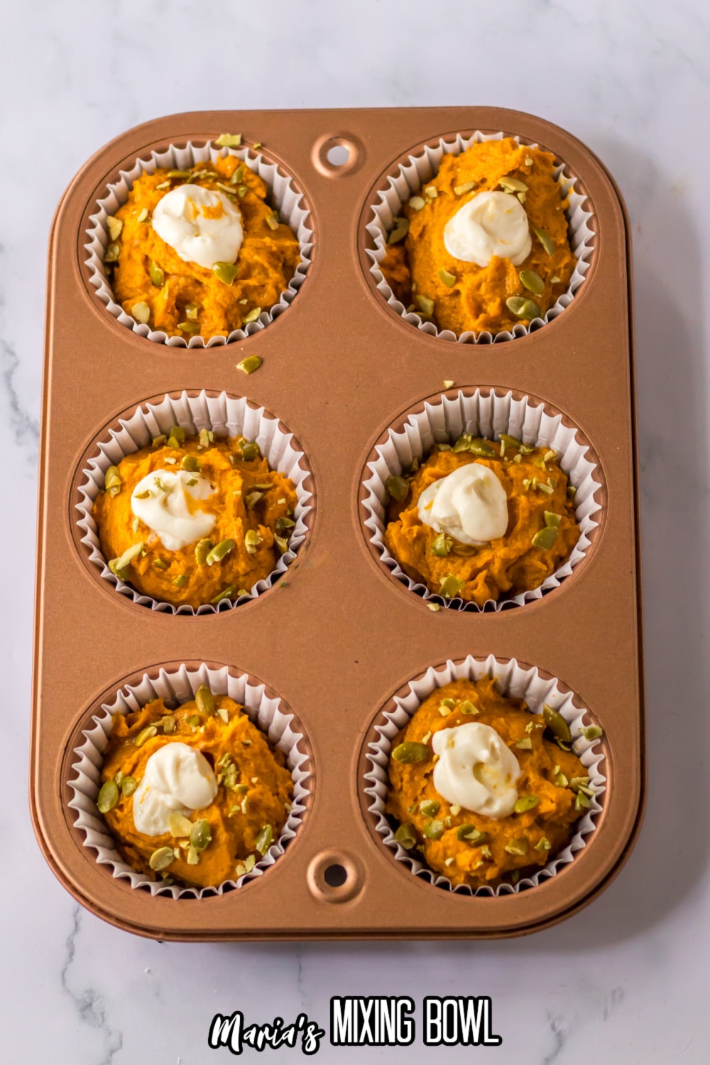 pumpkin muffin batter in a muffin pan with cream cheese in the center.