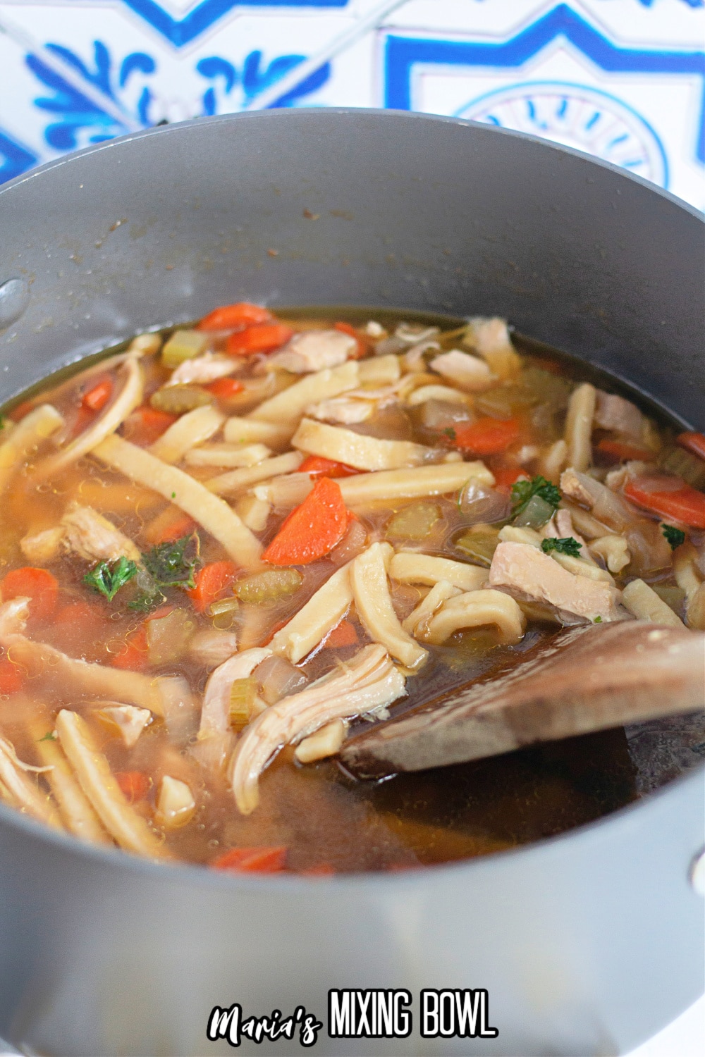 chicken noodle soup in a large stockpot with a wooden spoon