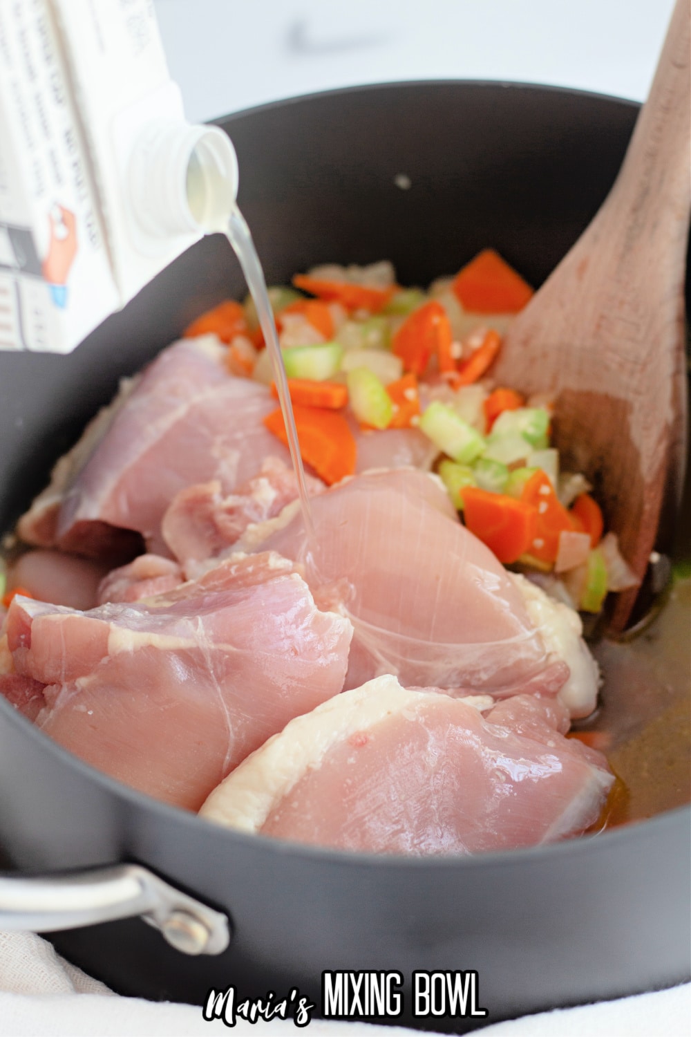 boneless skinless chicken thighs and chicken broth being added to a large pot with celery, carrots and onions