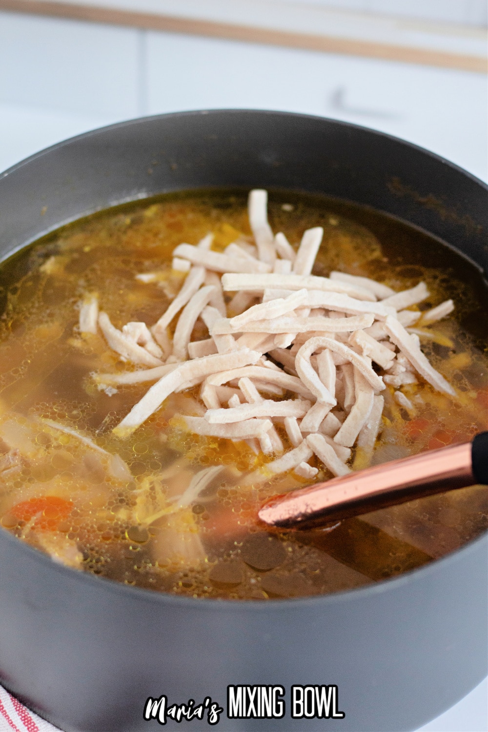 frozen noodles being added to a pot of chicken noodle soup