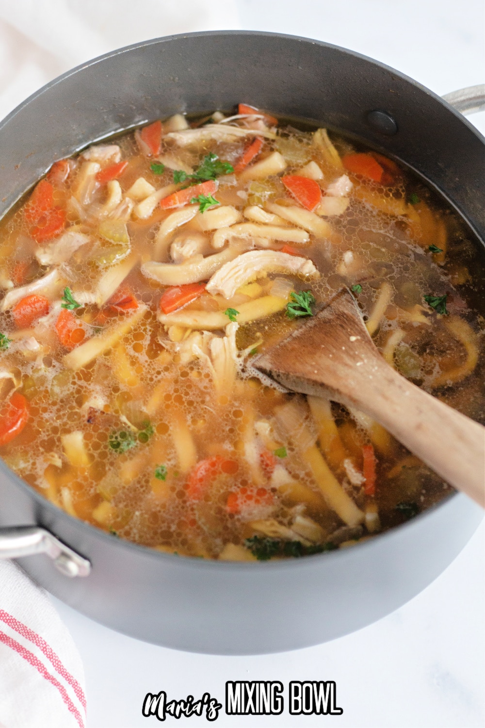 chicken noodle soup in a large stockpot with a wooden spoon