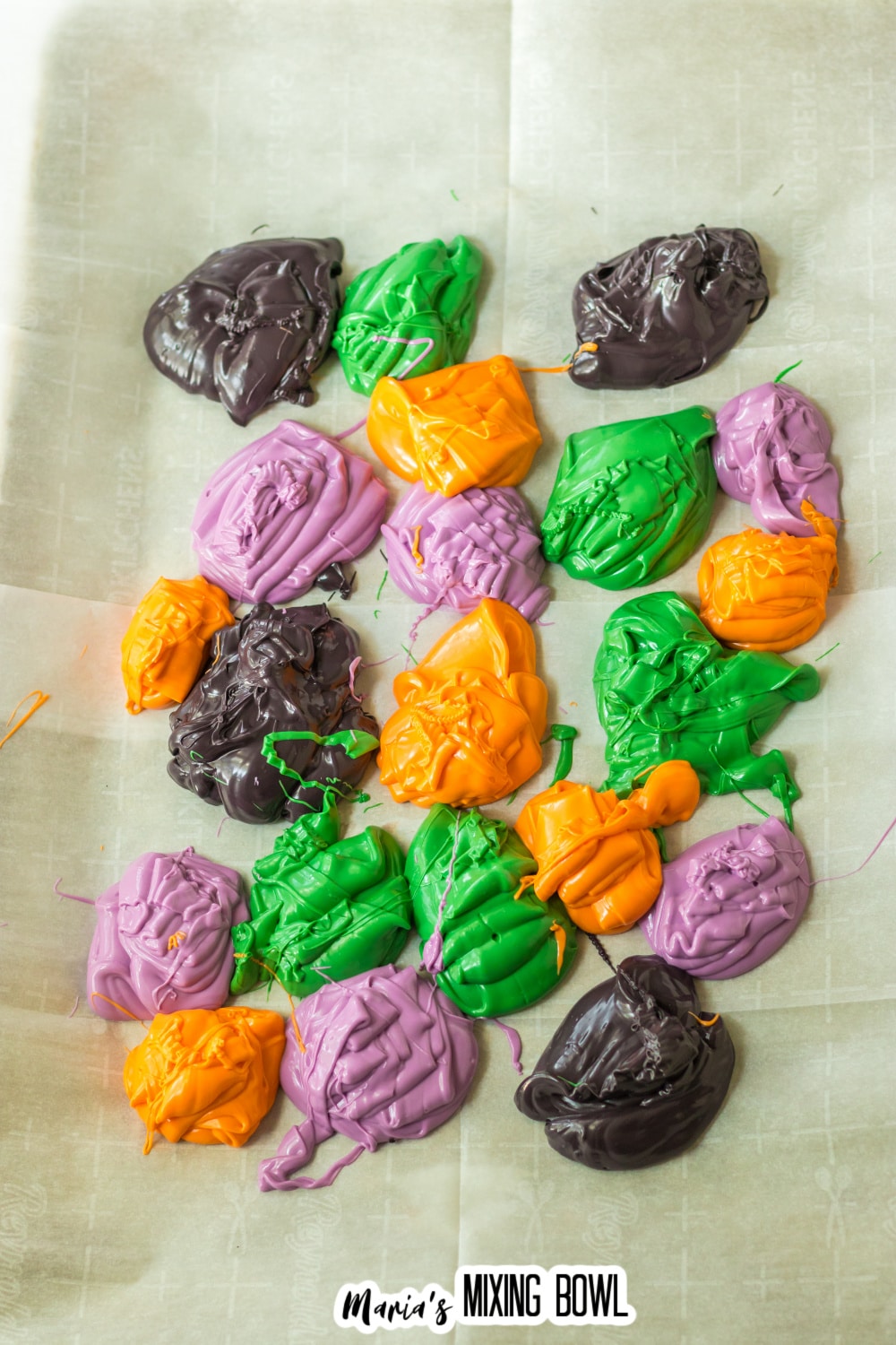 dollops of colored melted chocolate on a parchment lined baking sheet.