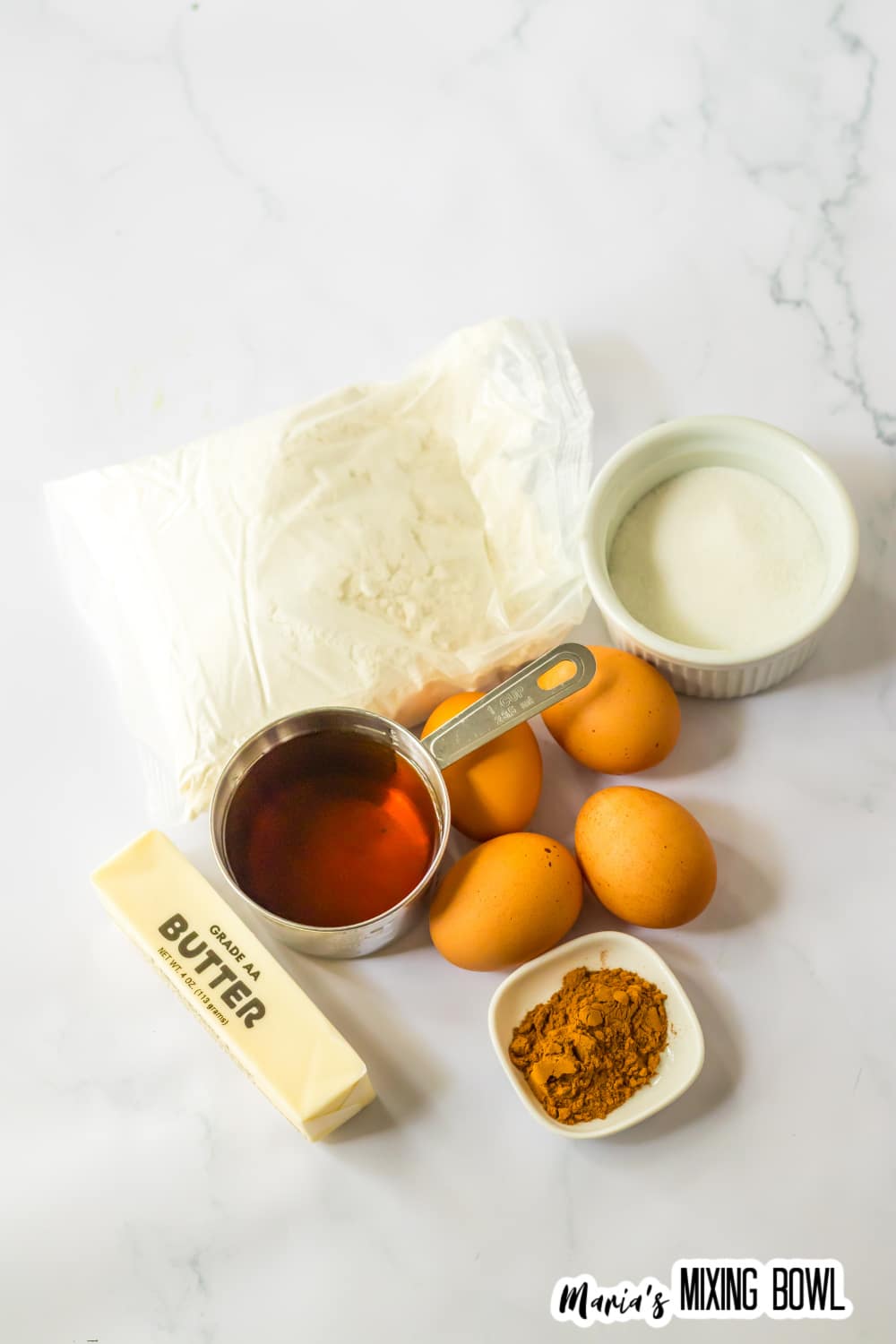 bag of cake mix, stick of butter, four eggs, small bowl of sugar, small bowl of cinnamon and a measuring cup filled with apple cider.