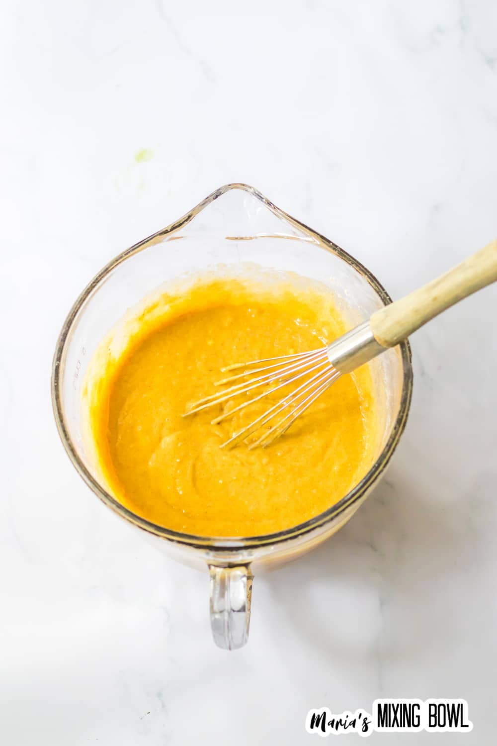 cake batter being mixed with eggs, melted butter, and apple cider in a glass mixing bowl with a whisk.