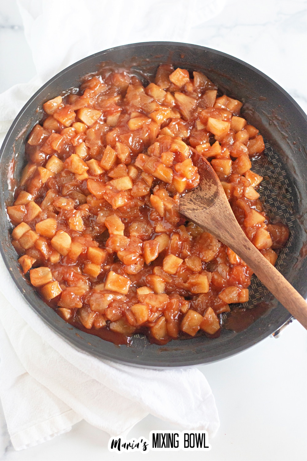 cooked apples being thickened in a skillet and stirred with a wooden spoon.