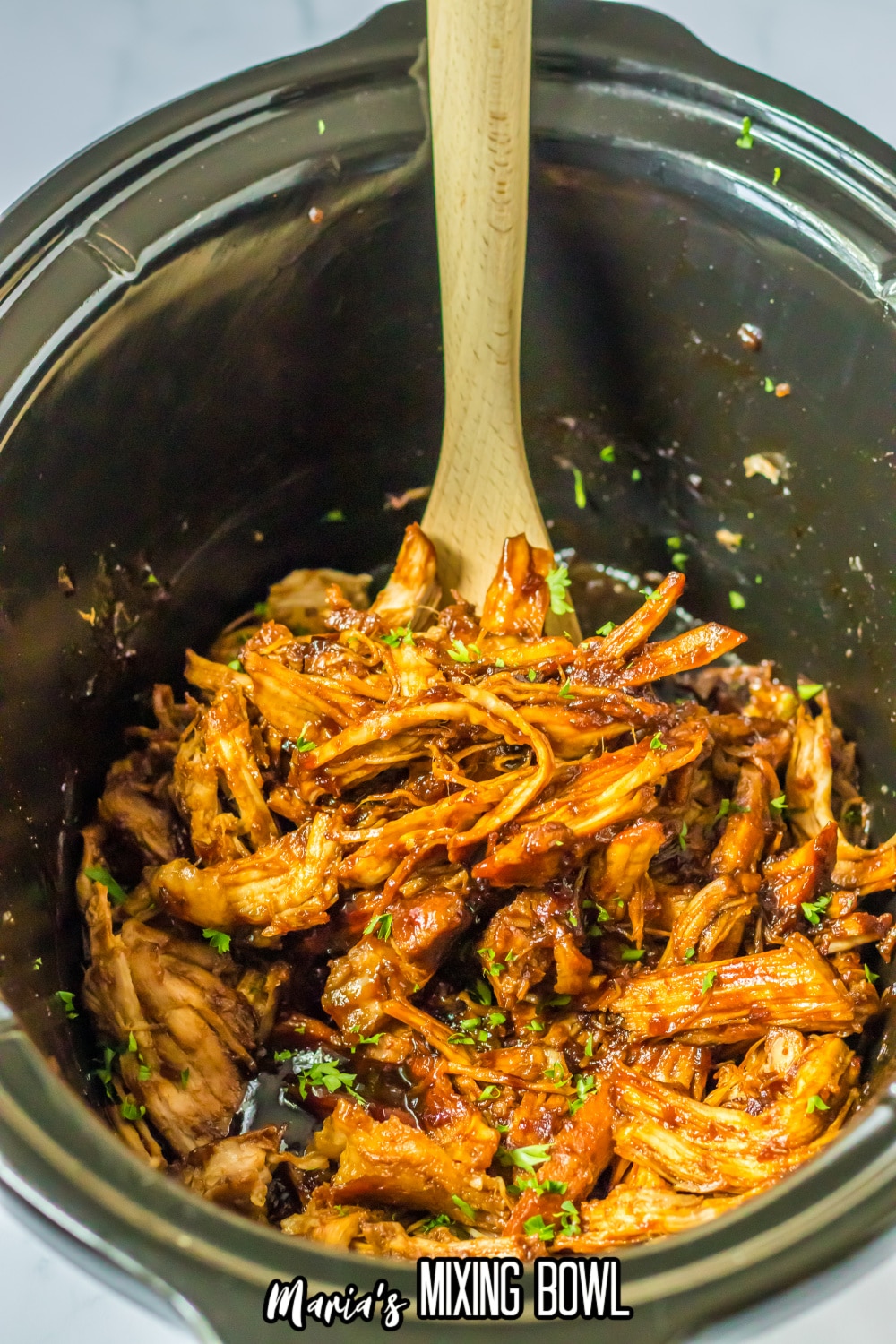 shredded pork loin in the crock to a slow cooker with a large wooden spoon.