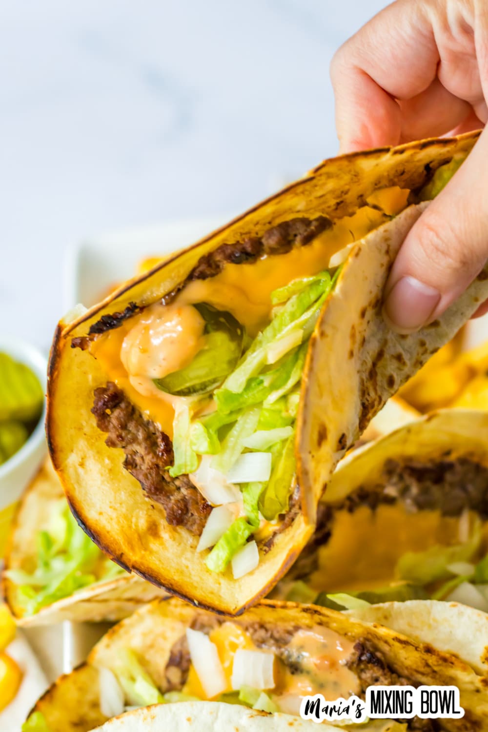 big mac taco held in a womans fingers in the air.