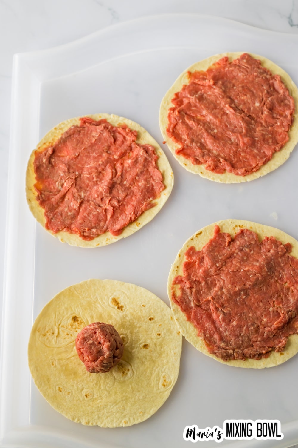 ground beef being spread on a tortilla.