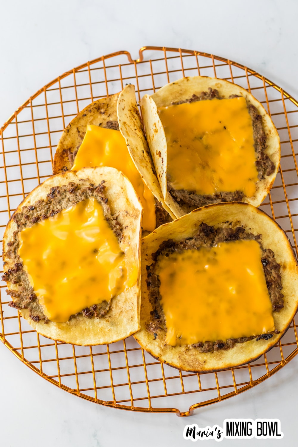 cheese being melted on top of smash burgers.