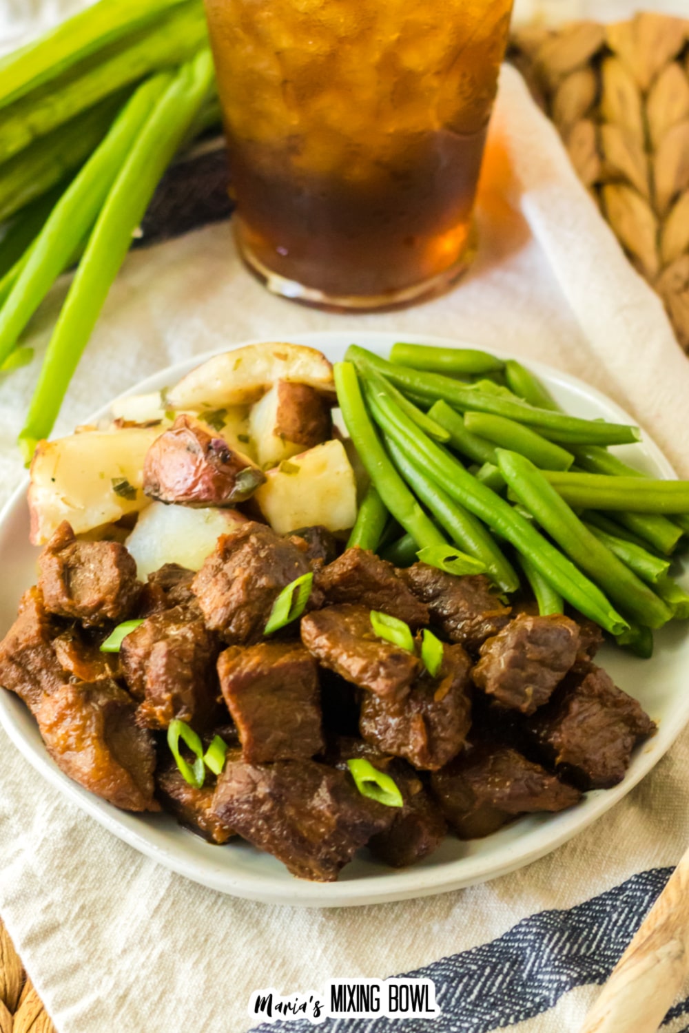 white plate filled with bourbon steak bites, cooked potatoes, and green beans.