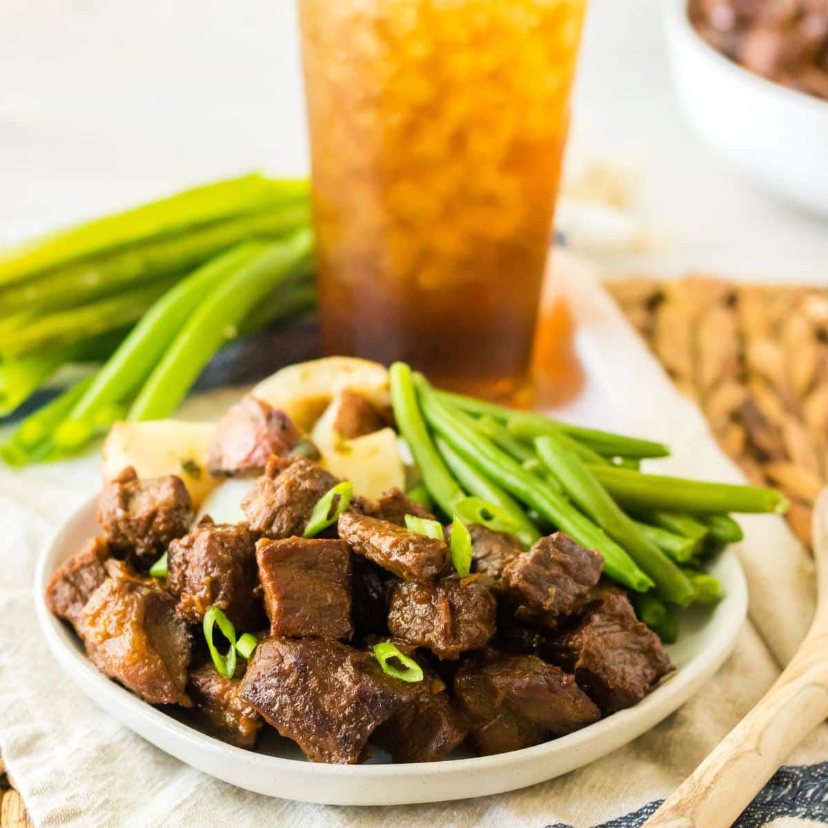 white plate filled with bourbon steak bites, cooked potatoes, and green beans.