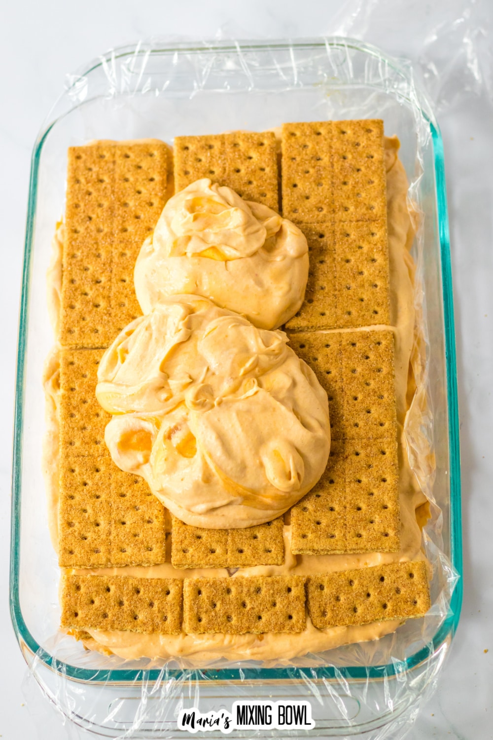 caramel apple filling being spread on top of graham crackers in a glass baking dish.