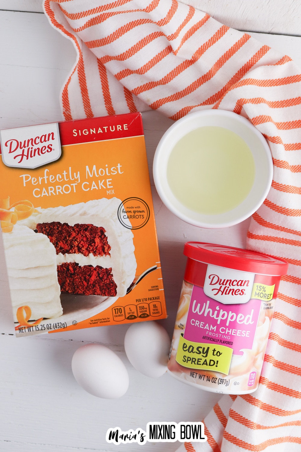 box of carrot cake mix, two eggs, container of whipped cream cheese frosting, and a small bowl of oil.