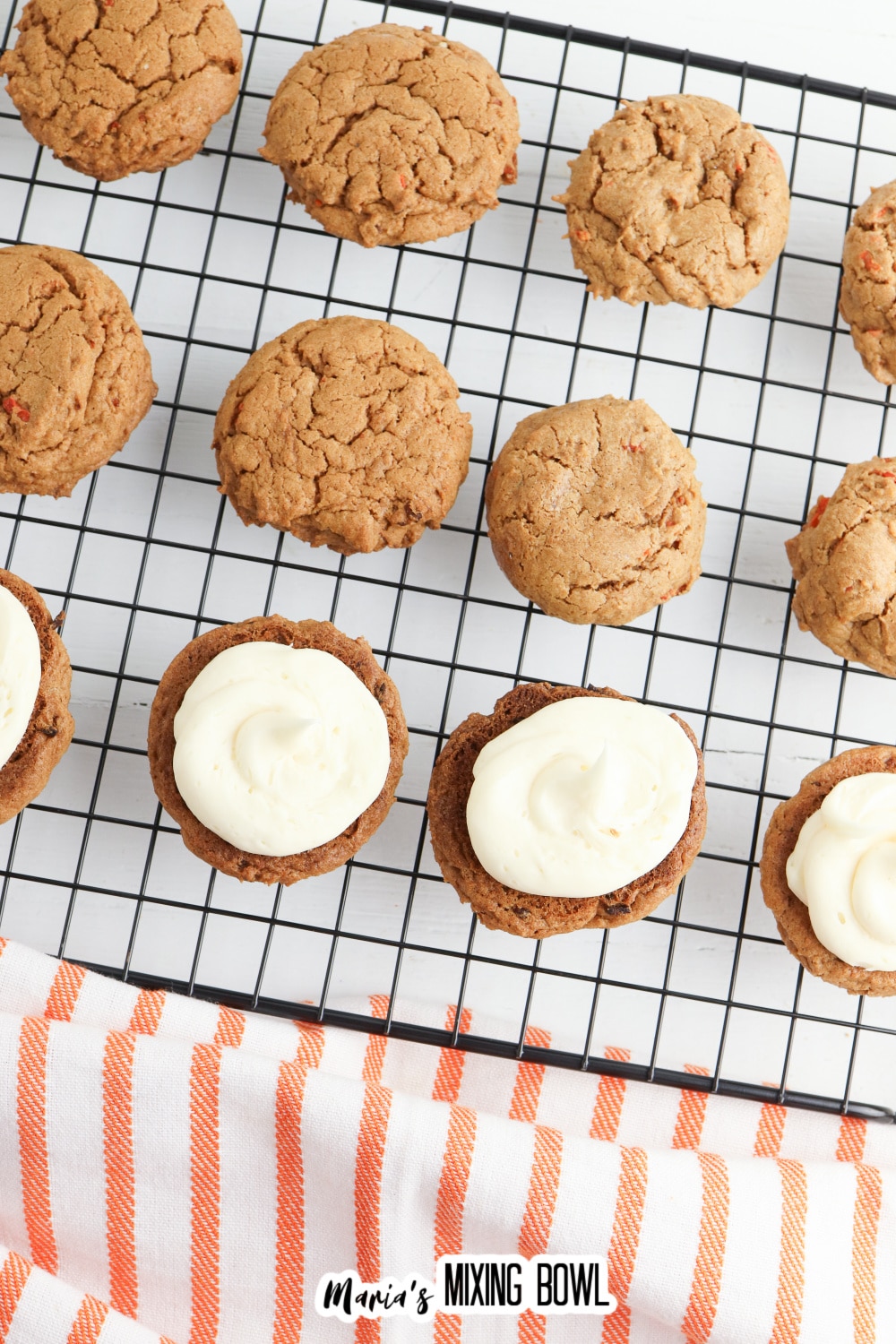 carrot cake mix cookies being filled with cream cheese frosting on a wire cooling rack.