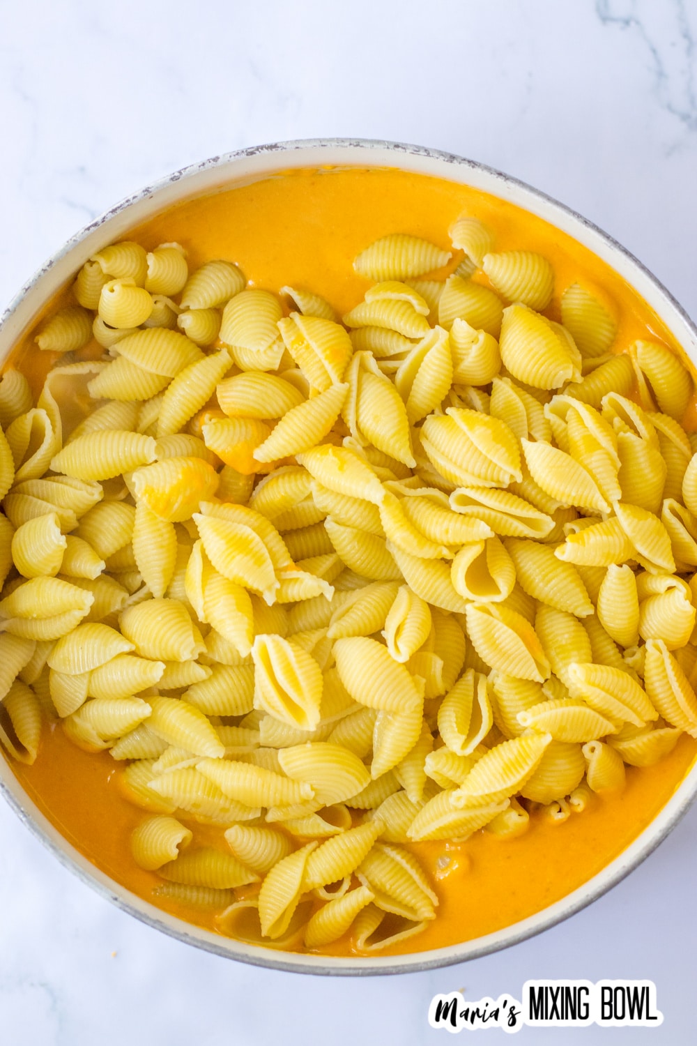 cooked pasta being added to the pumpkin cheese sauce.
