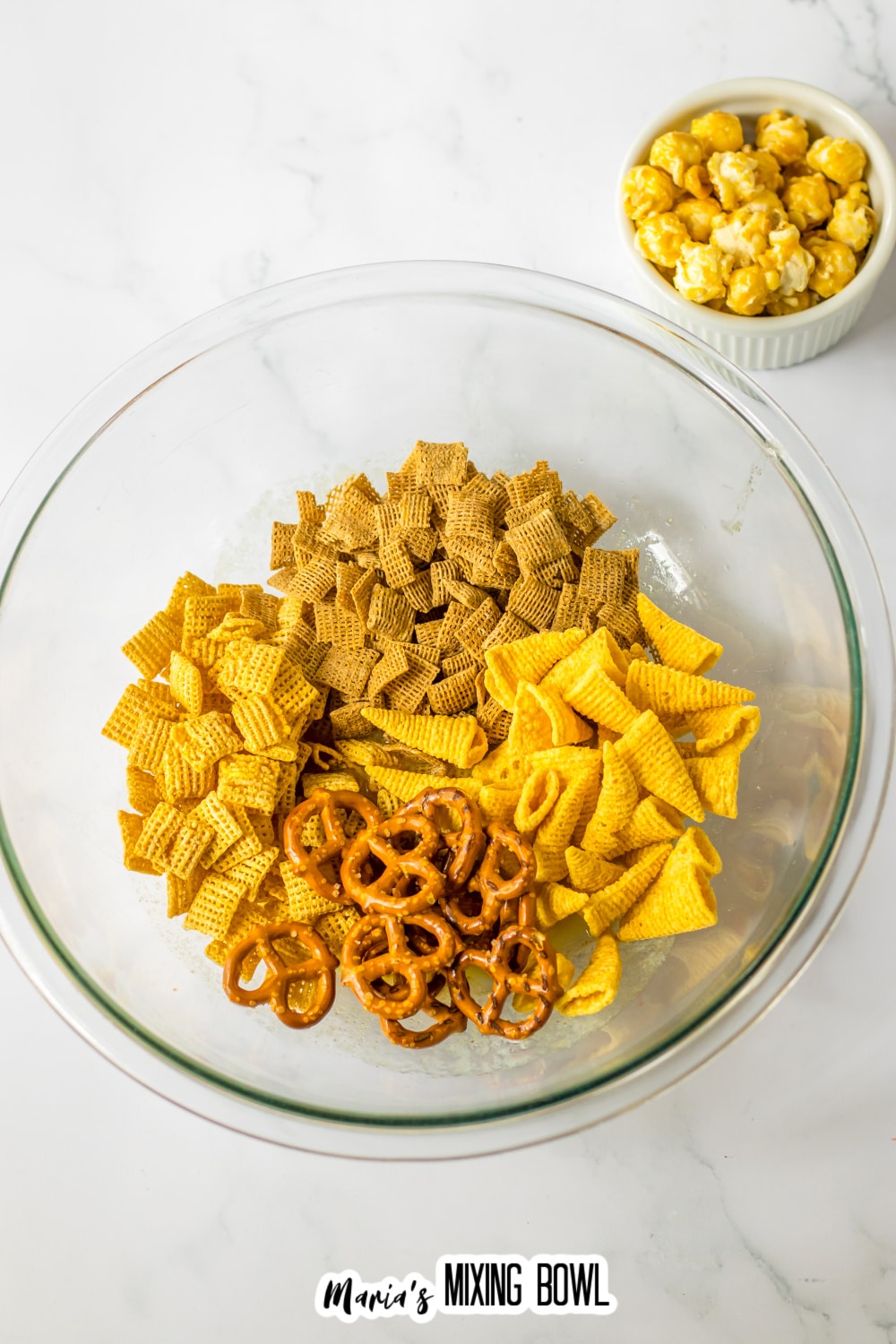 cereal, bugles, and pretzel in a glass mixing bowl.