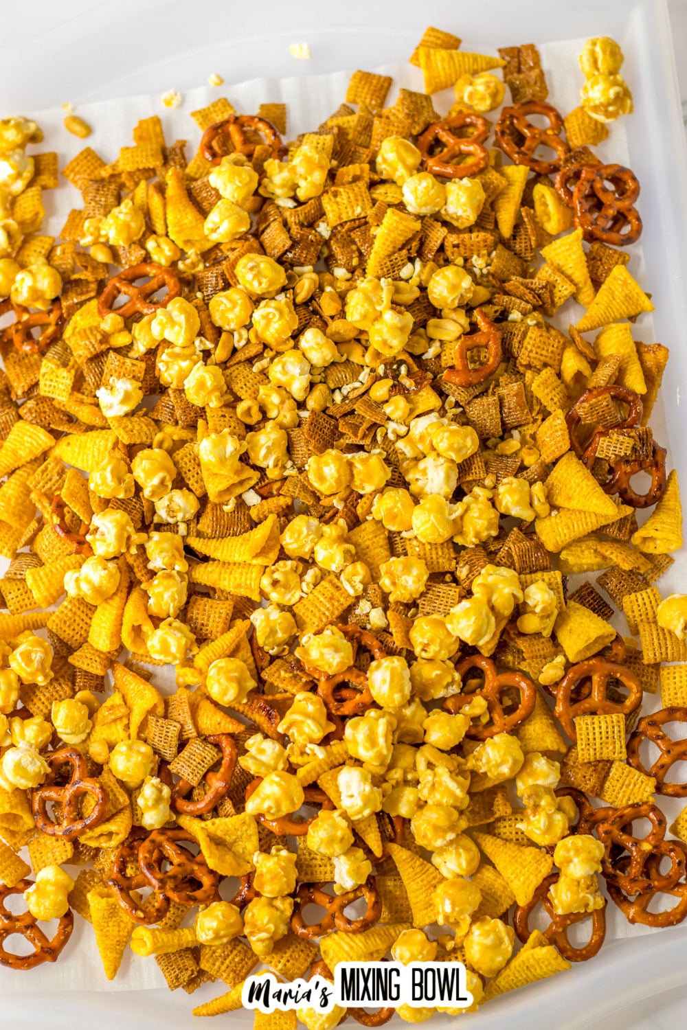 pretzels, chex cereal, bugles, and caramel corn drying on a parchment lined baking sheet
