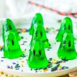seven green gelatin ghosts on a white plate with sprinkles.