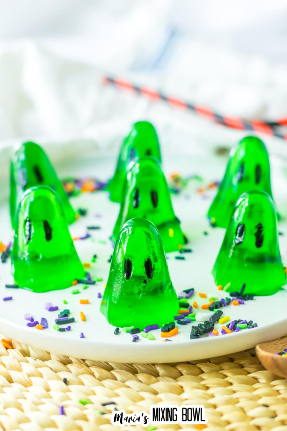 seven green gelatin ghosts on a white plate with sprinkles.