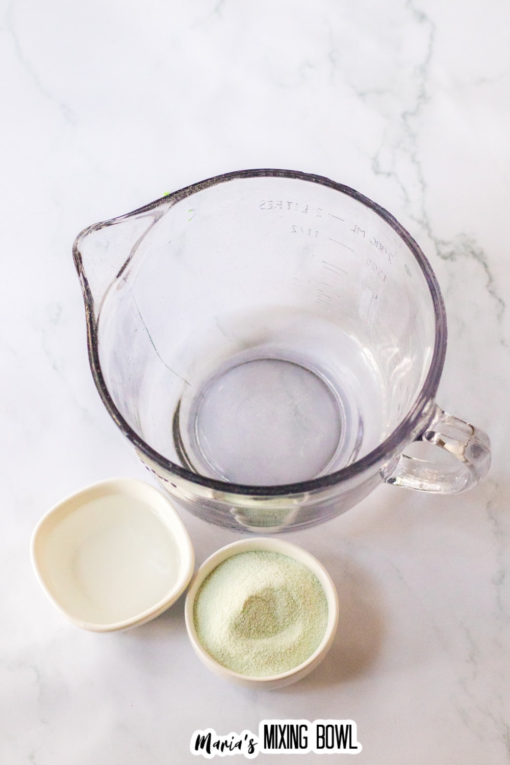 large mixing bowl, next bowls of water, and green gelatin powder.