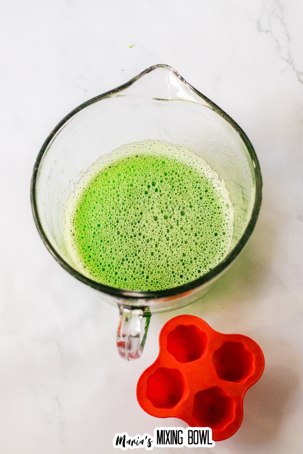 green gelatin being mixed with a water in a large measuring cup.