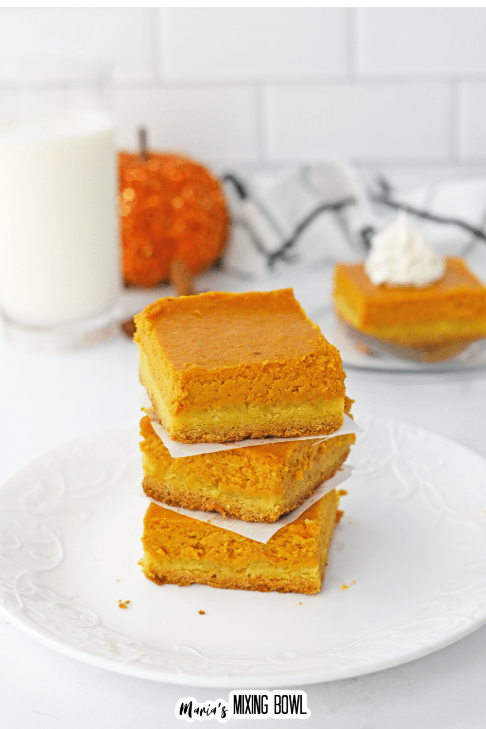three gooey pumpkin bars stacked on top of one another on a white plate.