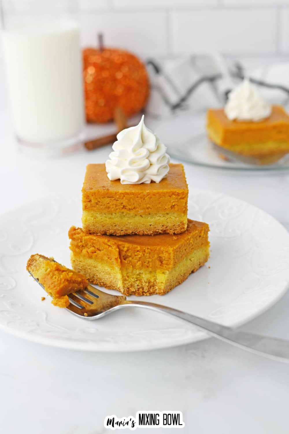 two gooey pumpkin bars stack on a plate with the bottom bar has a bite missing.