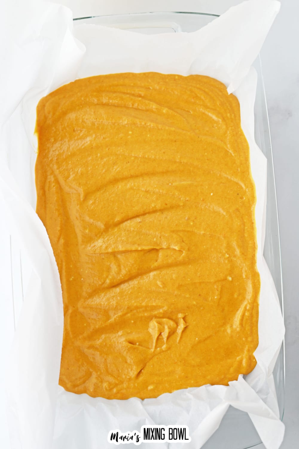 pumpkin bar dough in a glass baking dish in a parchment lined baking dish.