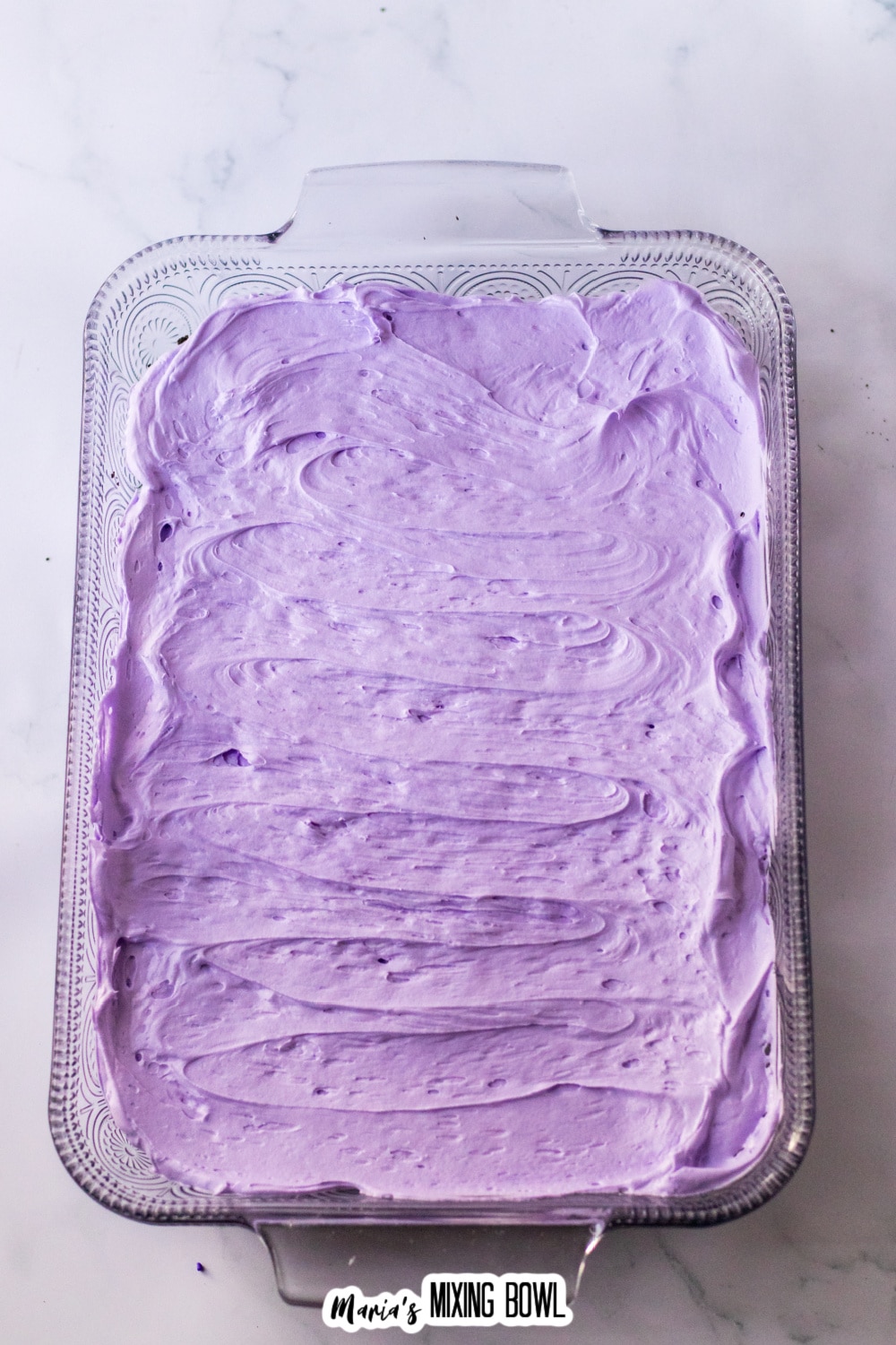 purple cream cheese layer being cream on top of Oreo cookie crush in a glass baking dish.